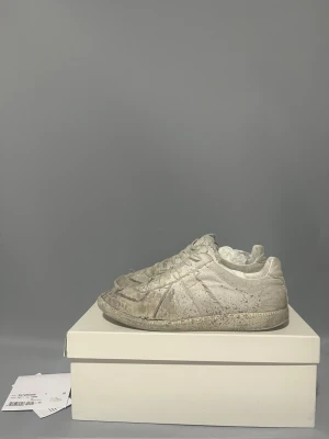 Maison margiela paint splatter ÄKTA‼️ - Maison Margiela sneakers i vit canvas med slitna detaljer och smutsad finish för en rå, vintage vibe. Klassisk rund tå, platt sula och snörning framtill. Snyggt distressed och unikt uttryck som sticker ut i mängden. Allt og äkta såklart storlek 43 finns defekter och hål