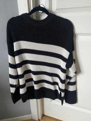 Svartvit randig stickad tröja - Säljer en svartvit stickad tröja med breda horisontella ränder. Tröjan har rund hals och långa ärmar, samt en loose passform som ger en chill vibe. Perfekt för dig som gillar klassiska mönster och vill ha något bekvämt och snyggt.