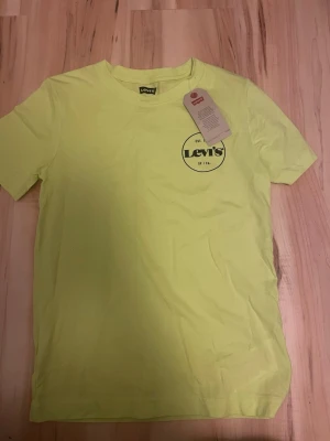 Gul Levi's t-shirt med logga - Fräsch gul t-shirt från Levi's med rund hals och tryckt logga på bröstet. Skön passform och tillverkad i mjuk bomull. Perfekt för dig som gillar färg och klassisk streetstyle.