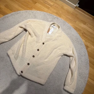 Vit kofta/Cardigan  - Mysig beige kofta från Topman med fluffig känsla och snygga bruna knappar framtill. Koftan har lång ärm och en klassisk v-ringad design. Perfekt för lager-på-lager och chill dagar. Passar dig som gillar en stilren och enkel look.
