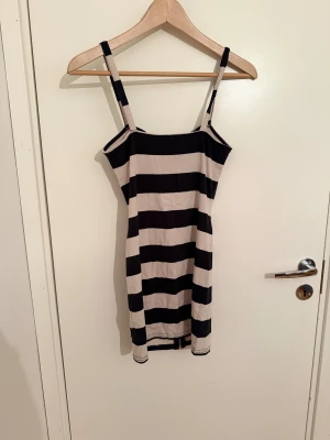 Randig kort klänning från H&M Divided - Snygg kort klänning från H&M Divided med breda svarta och beige ränder. Klänningen har smala axelband, figurnära passform och dragkedja framtill. Perfekt för dig som gillar en enkel men cool look.