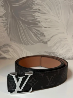 Svart bälte med silver logga - Svart bälte med silver logga, 115cm.