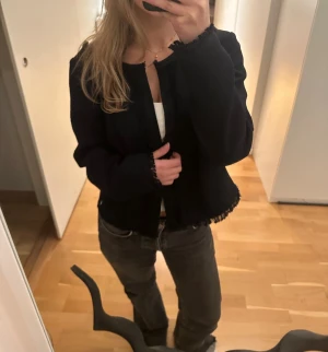 Mörkblå kofta / blazer  - Mörkblå kofta från Jette med lång ärm och detaljer längs hals och nederkant. Koftan är kortare i modellen och har två stycken hakknäppningar (istället för knappar eller dragkedja) 