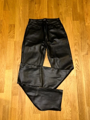 Svarta skinnbyxor från BikBok, strl 36 - Snygga svarta skinnbyxor från BikBok i storlek 36. Byxorna har klassisk femficksdesign, raka ben och midwaist passform. Materialet är syntetiskt skinn. Supersnygga på och formar sig efter kroppen. 