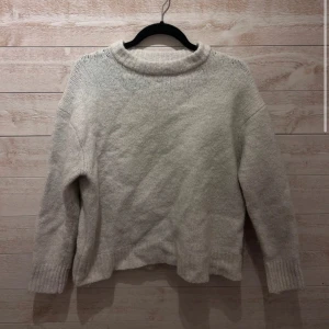 Ljusgrå stickad tröja från Zara - Mysig ljusgrå stickad tröja från Zara med rundad hals och ribbade muddar vid ärmslut och nederkant. Perfekt för kyliga dagar och enkel att matcha med jeans eller kjol. Tröjan har en loose passform och är långärmad.