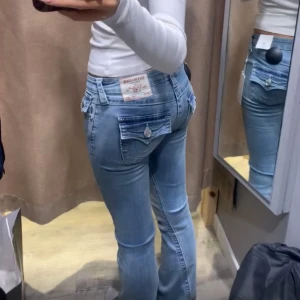 Ljusblå True Religion jeans bootcut - Säljer ett par ljusblå jeans från True Religion med bootcut och snygga detaljerade bakfickor med lock och silverknappar. Jeansen har låg midja och klassisk jeanslook i bomull. Perfekta för dig som gillar en avslappnad och trendig stil. De bild 3,4 för defekter 