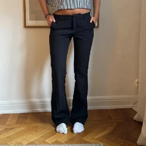 Lågmidjade kostymbyxor  - Snygga svarta kostymbyxor med bootcut passform och hällor för bälte. Byxorna har klassisk design med raka ben som blir vidare nedtill och sitter snyggt i midjan. Perfekta för en stilren look.