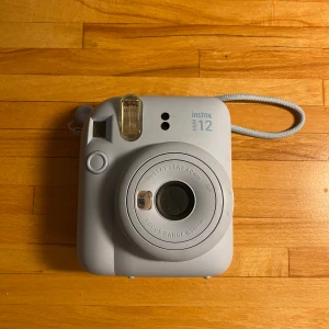 Instax Mini 12 ljus blå - Fujifilm Instax Mini 12 i ljusblått, kompakt och lättanvänd direktkamera. Utrustad med 60mm lins och inbyggd blixt. Kameran är i gott skick. Kommer inte med filmer. Ny pris är 900. Kontakta för mer info.