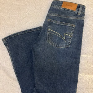 Blå jeans från Junkyard, storlek S - Klassiska blå jeans från Junkyard med snygga kontrastsömmar och unik bakficka med broderad detalj. Modellen har normal passform, fem fickor och bälteshällor. Perfekta för dig som gillar en enkel men stilren look. Använd få tal gånger, säljer då dom aldrig kommer till användning.