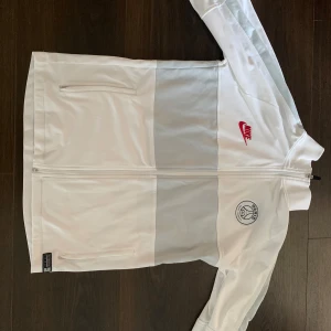 Vit Nike PSG tröja - Snygg vit tröja från Nike x Paris Saint-Germain med röd Nike-logga och PSG-märke på bröstet.