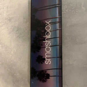 Smashbox ögonskuggspalett med spegel - Snygg ögonskuggspalett från Smashbox med 16 olika färger, allt från neutrala beige och bruna toner till färgstarka nyanser som blått, lila, guld och rött. Paletten har en stor spegel och kommer i ett stilrent fodral med palmmotiv.