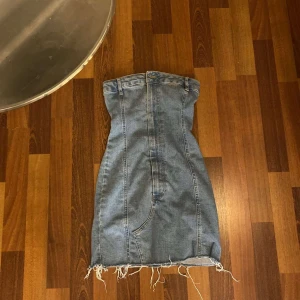 Jeansklänning från Pull&Bear XS - Säljer min absoluta favorit jeansklänning från Pull&Bear i storlek XS. Klänningen är kort, har råa fransiga kanter nertill och markerade sömmar för en cool look. Gjord i klassisk blå denim med fickdetaljer och knapp framtill.