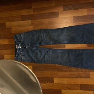 Blå bootcut jeans från Nelly - Säljer ett par blå jeans från Nelly med bootcut-modell och snygga kontrastsömmar. Jeansen har medelhög midja och klassiska bakfickor med broderad detalj. Perfekta för dig som gillar en snygg look och vill ha ett par jeans som sticker ut lite extra.