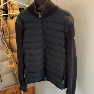Svart pufferjacka från Moncler - Snygg svart moncler cardigan med quiltad framsida och släta ärmar. Jackan har hög krage, tvåvägsdragkedja och dragkedjeförsedda fickor. Perfekt för dig som vill ha en stilren och exklusiv look. Storlek L men sitter som M