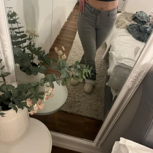 Gråa raka jeans med låg midja - Säljer ett par gråa jeans med låg midja och boot ben. Jeansen har klassisk femficksdesign, bälteshällor och dragkedja med knapp. Snygg passform som sitter tajt upptill och släpper lite vid benen. Perfekta till sneakers eller boots.