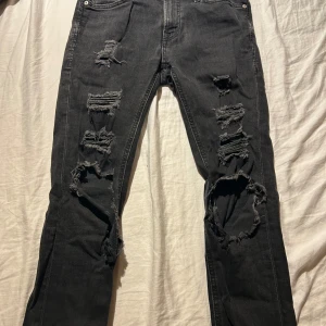 Svarta skinny jeans Jack & Jones - Svarta skinny jeans från Jack & Jones, modell Liam. Riktigt slitna med stora hål och trasiga detaljer på båda benen för en edgy look. Klassisk femficksmodell i stretchig bomullsdenim. Perfekta för dig som gillar streetstyle och vill sticka ut.