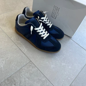 Maison Margiela sneakers blå - Snygga Maison Margiela sneakers i marinblå mocka och skinn med vita snören och beige sula. Klassisk siluett med rund tå och platt sula, perfekt för dig som gillar stilrena och exklusiva sneakers. Märkesdetaljer på plösen och insidan.
