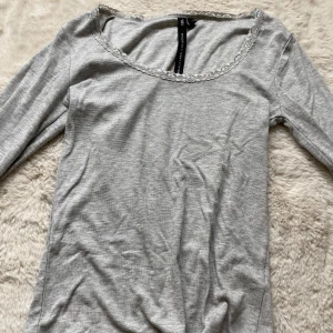 Grå långärmad topp med spetskant - Grå långärmad topp från H&M med rundad halsringning dekorerad med söt spetskant. Tillverkad i mjuk bomullsmix som känns skön mot huden. Perfekt för lager-på-lager och enkel att matcha med jeans eller kjol.