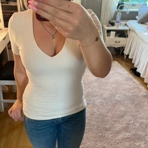 Vit v-ringad topp med kort ärm - Säljer en stilren vit topp med v-ringning och korta ärmar. Toppen har en figurnära passform och är tillverkad i ett mjukt bomullsmaterial som känns skönt mot huden. Perfekt att matcha med jeans eller kjol för en enkel och snygg look.