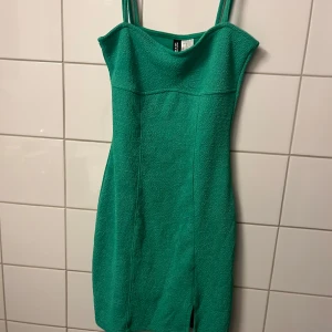 Grön kort klänning från Gina Tricot - Snygg grön klänning med smala axelband och figurnära passform. Klänningen är kort och har en liten slits framtill🌸🌸.