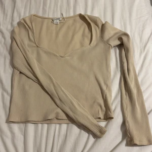 Beige ribbad topp från Monki - Säljer en beige långärmad topp från Monki i storlek S. Toppen är ribbad med v-ringad halsringning och har en figurnära passform. Väldigt low cut så perfekt om man vill visa cleavage