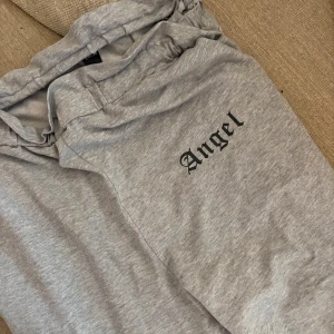 Grå mjukisbyxor med tryck Angel - Snygga grå mjukisbyxor med svart texten 'Angel' tryckt på ena benet. Byxorna har resår i midjan.