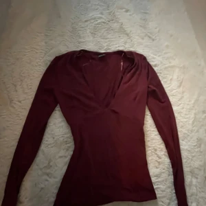 Vinröd omlottopp från Gina Tricot - Säljer en vinröd omlottopp från Gina Tricot i storlek XS. Toppen har lång ärm, djup v-ringning och figurnära passform.Den är aldrig använd bara testat och utan lapp😊