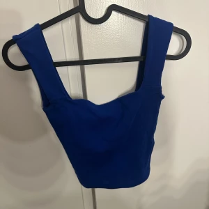 Kornblå croppad topp från Gina Tricot - Säljer en kornblå croppad topp från Gina Tricot i storlek XS. Toppen har breda axelband och fyrkantig urringning både fram och bak. Tillverkad i mjuk bomullsmix som sitter tight och bekvämt. Perfekt att styla med höga jeans eller kjol.