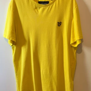 Gul t-shirt från Lyle & Scott - Fräsch gul t-shirt från Lyle & Scott med klassisk passform och ikonisk logga på bröstet. Tillverkad i mjuk bomull och har rund hals samt korta ärmar. Perfekt för dig som vill sticka ut med färg och enkel stil.