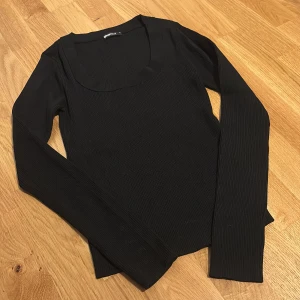 Svart ribbad långärmad topp Gina Tricot - Svart långärmad topp från Gina Tricot med ribbad struktur och rundad, djup ringning. Snygg och enkel modell som är lätt att matcha till olika outfits. Perfekt basplagg för garderoben.