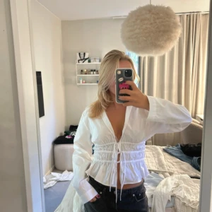 Vit omlott skjorta med snörning från Zara - Säljer en vit skjorta från Zara med snygg snörning i midjan och omlott-design. Skjortan har lång ärm, krage och volangdetalj nedtill. Perfekt för dig som gillar trendiga och feminina plagg med lite edge. Aldrig använd med prislappar kvar!