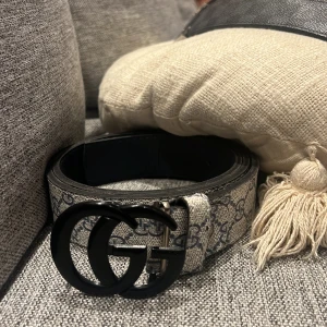 Bälte med GG-monogram - Ett beige bälte med GG-monogram och ett svart GG märke, bältet är väldigt snyggt och manligt, perfekt till dig som vill se lite mognare ut och äldre. Passar mycket till ortenstilen, grisch och även kostym