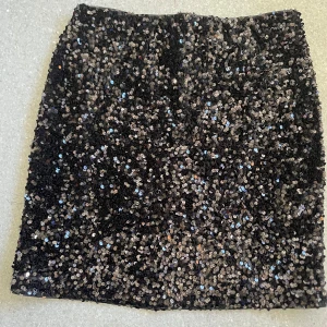 Svart paljettkjol från Carin Wester - Glittrig svart midikjol från Carin Wester, täckt med paljetter som ger en riktigt festlig vibe. Kjolen har rak passform och är fodrad för extra komfort. Perfekt för dig som vill sticka ut med en snygg och trendig look.