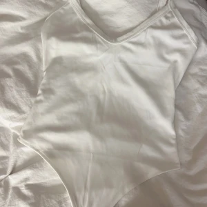 Vit body från Shein - Säljer en body från SHEIN med smala axelband och v-ringning. Toppen är tillverkad i mjuk och stretchig polyesterblandning som sitter snyggt på kroppen. Perfekt att matcha med jeans eller kjol.