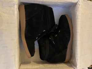 Svarta sneakers med kilklack från Pavement - Säljer ett par svarta sneakers från Pavement i storlek 37. Skorna har en kilklack, snörning och är gjorda i skinn med mockakänsla. Yttersulan är beige och ger en snygg kontrast mot det svarta. Perfekt för dig som vill ha lite extra höjd men ändå bekvämt.🙏🏽🥰