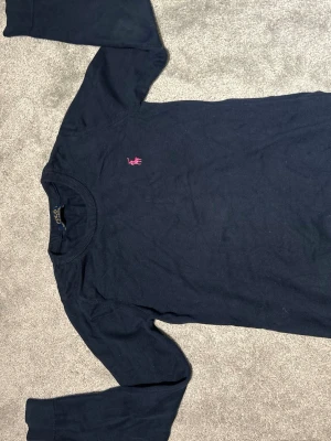 Mörkblå långärmad tröja Polo Ralph Lauren - Snygg mörkblå långärmad tröja från Polo Ralph Lauren i 100% bomull. Klassisk rund hals och rosa broderad logga på bröstet. Perfekt för dig som gillar stilrena och tidlösa plagg med en sportig touch.