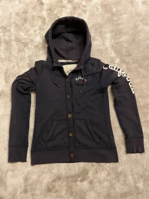 Hollister hoodie mörkblå - Mörkblå hoodie från Hollister med tryck och vit markerad text på höger arm ”California” | Storlek S/M | Armhåla neråt 40 cm | Armlängd 69 cm | Passar för 165-176 cm | Hör gärna av dig vid frågor eller funderingar | Pris kan alltid diskuteras|