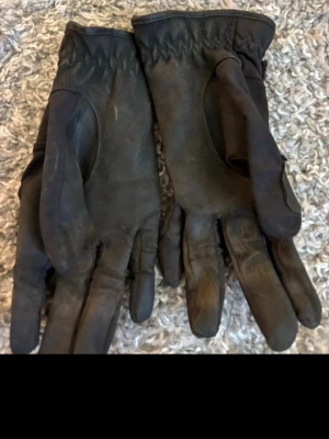 Svarta ridhandskar från Jacson, M - Säljer ett par svarta ridhandskar från Jacson i storlek M. Handskarna har justerbar kardborre med Jacson-logga, förstärkta partier och är tillverkade i syntetmaterial med detaljer i skinn. Perfekta för ridning och har en snygg, sportig look.