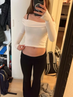 Vit offshoulder croppad topp - Säljer en vit, croppad topp med offshoulder-design och långa ärmar. Toppens stil är enkel och fräsch, med en bred krage som ligger snyggt över axlarna. Materialet känns mjukt och stretchigt, perfekt för dig som gillar en slim passform och vill visa lite midja. Fråga mig om ni undrar något😊