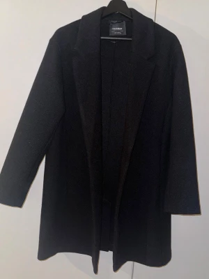 Svart kappa från Pull&Bear, S - Svart stilren kappa från Pull&Bear i storlek S. Klassisk rak modell med krage och långa ärmar, perfekt för dig som gillar minimalistisk look. Materialet känns mjukt och har en ullig känsla. Enkel att matcha med olika outfits.