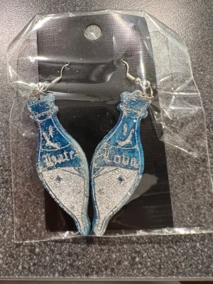 Blåa Trolldrycksflaskor örhängen - Blåa Trolldrycksflaskor örhängen med texten 'Hate' och 'Love', i blått och silver med glitter. Perfekt för häxor 