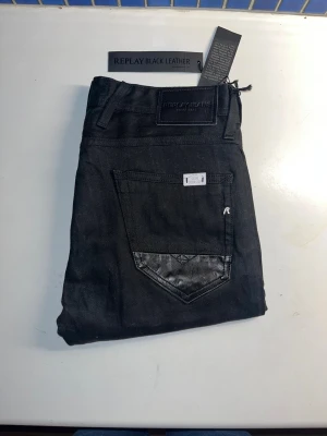 Replay Anbass jeans - Helt nya svarta Replay Anbass jeans med slim passform och snygga detaljer i svart läder på bakfickorna. Materialet är jeans med inslag av läderdetaljer, vilket ger en cool och modern vibe. Midja 39cm, längd 112cm. Ifall det inte finns någon bild i annonsen där jag bär plaggen jag säljer så är det för att jag ej kan ha storleken heller passformen, så kolla måtten för storlek och googla på modellnamnet för passform 😉76