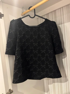 Svart blus med rosettmönster från Vila - Säljer en svart blus från Vila i storlek 40/L/ XL. Blusen har ett snyggt rosettmönster över hela tyget och halvlånga ärmar. Rund halsringning och lätt A-linjeformad siluett. Perfekt för dig som gillar detaljer och vill ha något som sticker ut.