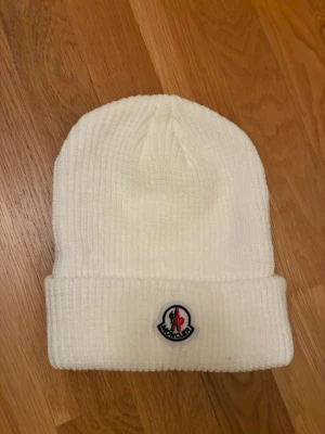 Vit moncler mössa - Bilderna visar en vit ribbad mössa från Moncler, inte en väst. Mössan har ett uppvikt kant och Moncler-logga framtill.