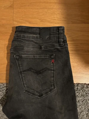 Replay svarta slim jeans - Säljer ett par svarta Replay jeans med slim passform och klassisk femficksdesign. Jeansen har en diskret tvättad look, röd Replay-logga på bakfickan och svarta sömmar. Perfekt för dig som gillar stilrena och moderna jeans.