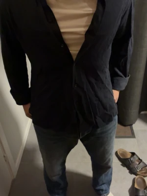 Svart skjorta från Eton, storlek M - Säljer en svart skjorta från Eton i storlek M. Skjortan har klassisk krage, långa ärmar och knäppning framtill. Materialet känns lätt och andas bra, perfekt för dig som gillar stilrena och enkla plagg. Passar dig som vill ha en clean look.