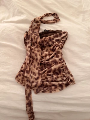 Leopardmönstrad bandeau tubtopp - Säljer en leopardmönstrad bandeau tubtopp från Zara med bruna och beige toner. Toppen är axelbandslös med snygga rynkade detaljer och ett matchande knytband.