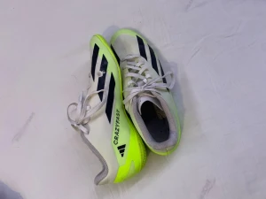 Adidas Crazyfast vita och neongula inomhusskor - Säljer ett par Adidas Crazyfast fotbollsskor i vitt och neongult med svarta detaljer. Skorna har snörning och en platt sula som är märkt 'non marking'. Materialet är syntet och mesh, och designen är sportig med tydliga Adidas-ränder på sidorna.