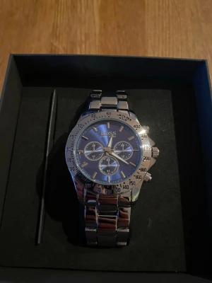 Hugo boss klocka - Bilderna visar en silvrig klocka från Hugo Boss med blå urtavla och metallarmband. Aldrig använd 