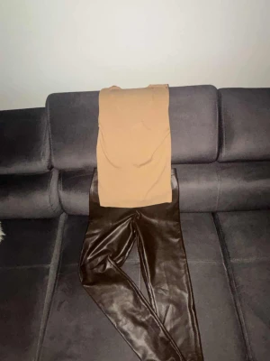 Bruna skinnleggings med slim passform - Snygga bruna leggings i skinnimitation med slim passform. De har en stilren look och sitter tajt längs benen, vilket ger en cool vibe. Perfekta att matcha med en oversized tröja eller hoodie för en trendig outfit.